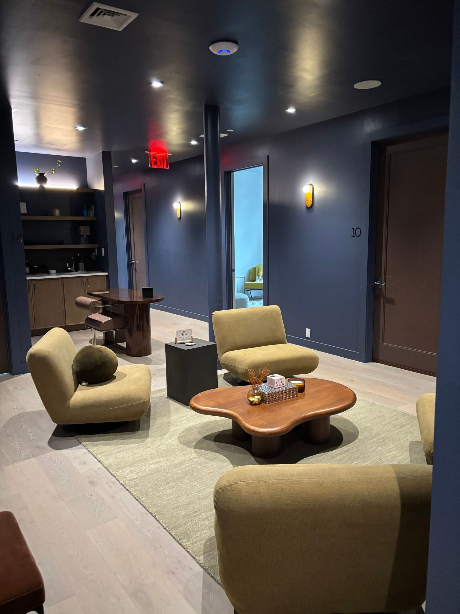 Office lounge with deep blue walls, upholstered chairs, and a wooden coffee table
