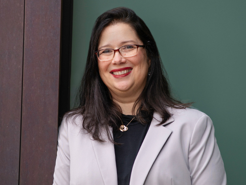 Suzanne Marmo smiling, wearing glasses and a light blazer