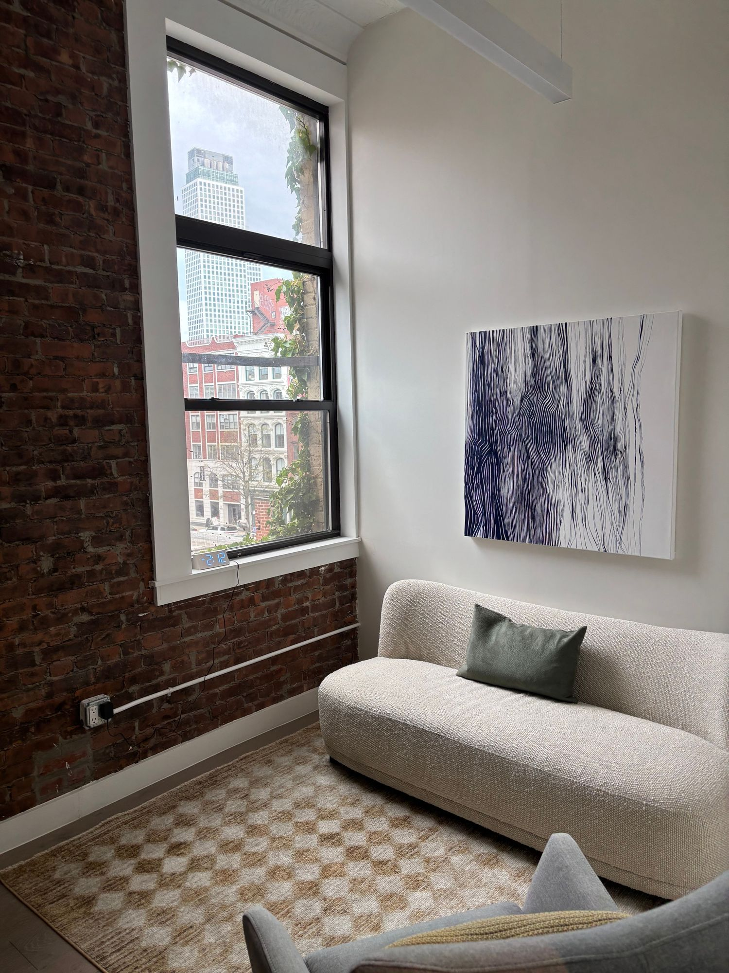 Light-filled therapy room with exposed brick, a large window, cream sofa, and abstract artwork